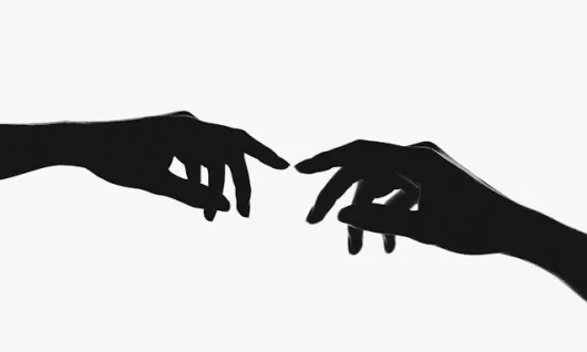 attachment_anderson-rian-uIE9f6gV8rI-unsplash Two hands reaching out to each other from either side of the image (almost touching their index fingers) to make a connection. They are black in shadow with a white background.