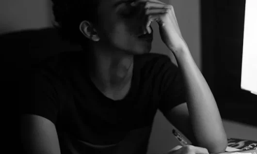 destructive_thought-patterns_sujin-c-QJrgVKyRT4A-unsplash Woman with hair back sitting at a desk in front of a screen with a pen in one hand over papers and the other covering part of her face (eyes closed) in a gesture of overwhelm.